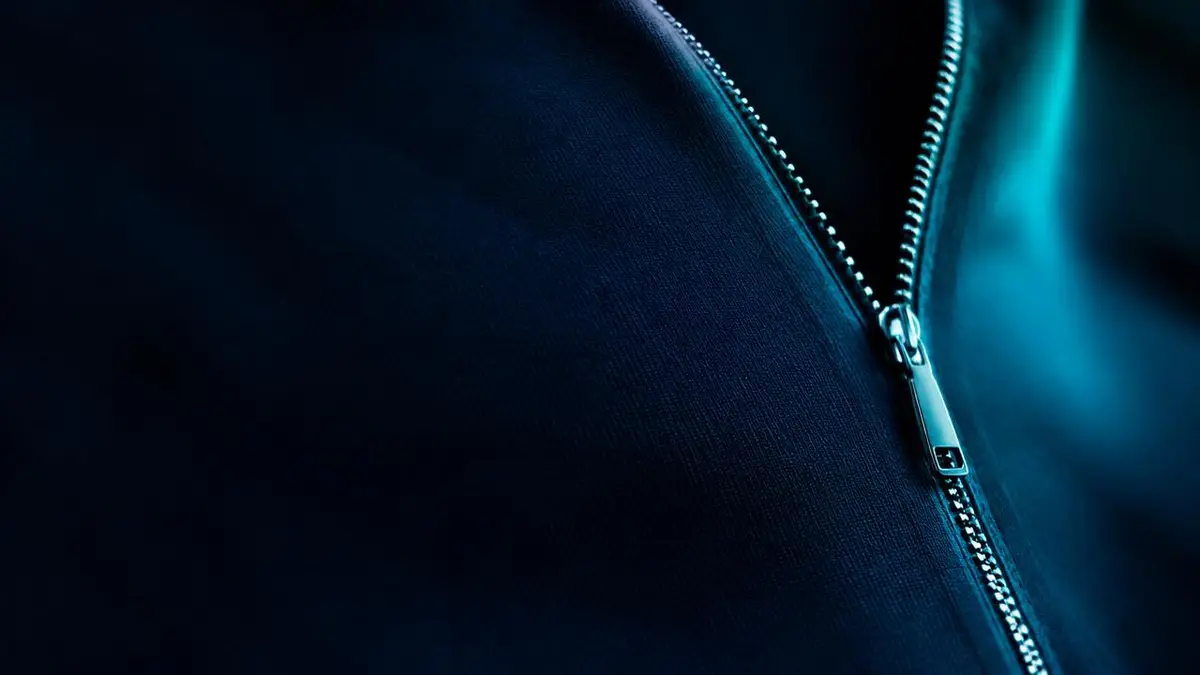 Close-up of a sleek metal zipper on navy fabric with teal light